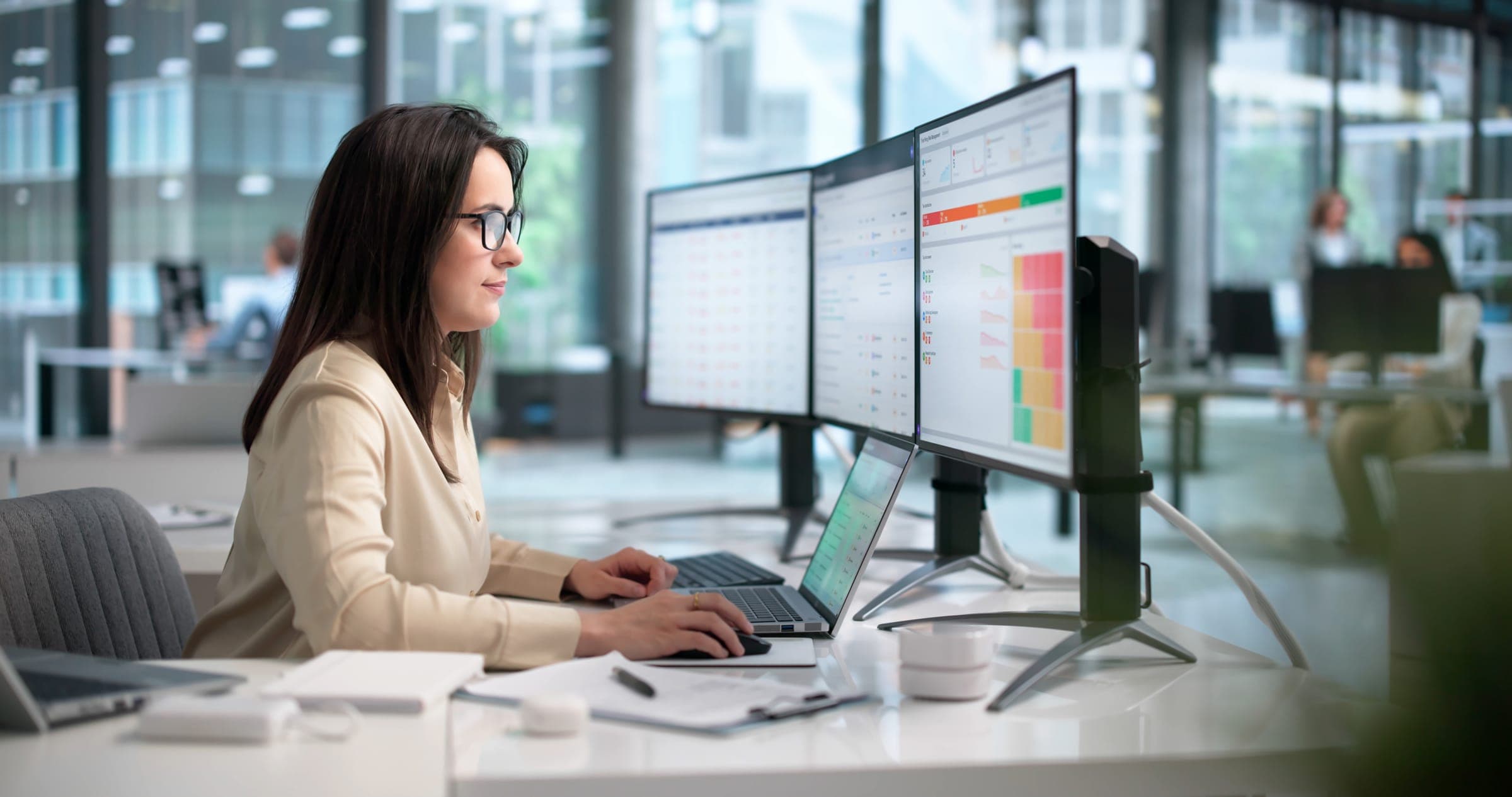 A professional working at a laptop and a row of monitors in an open office
