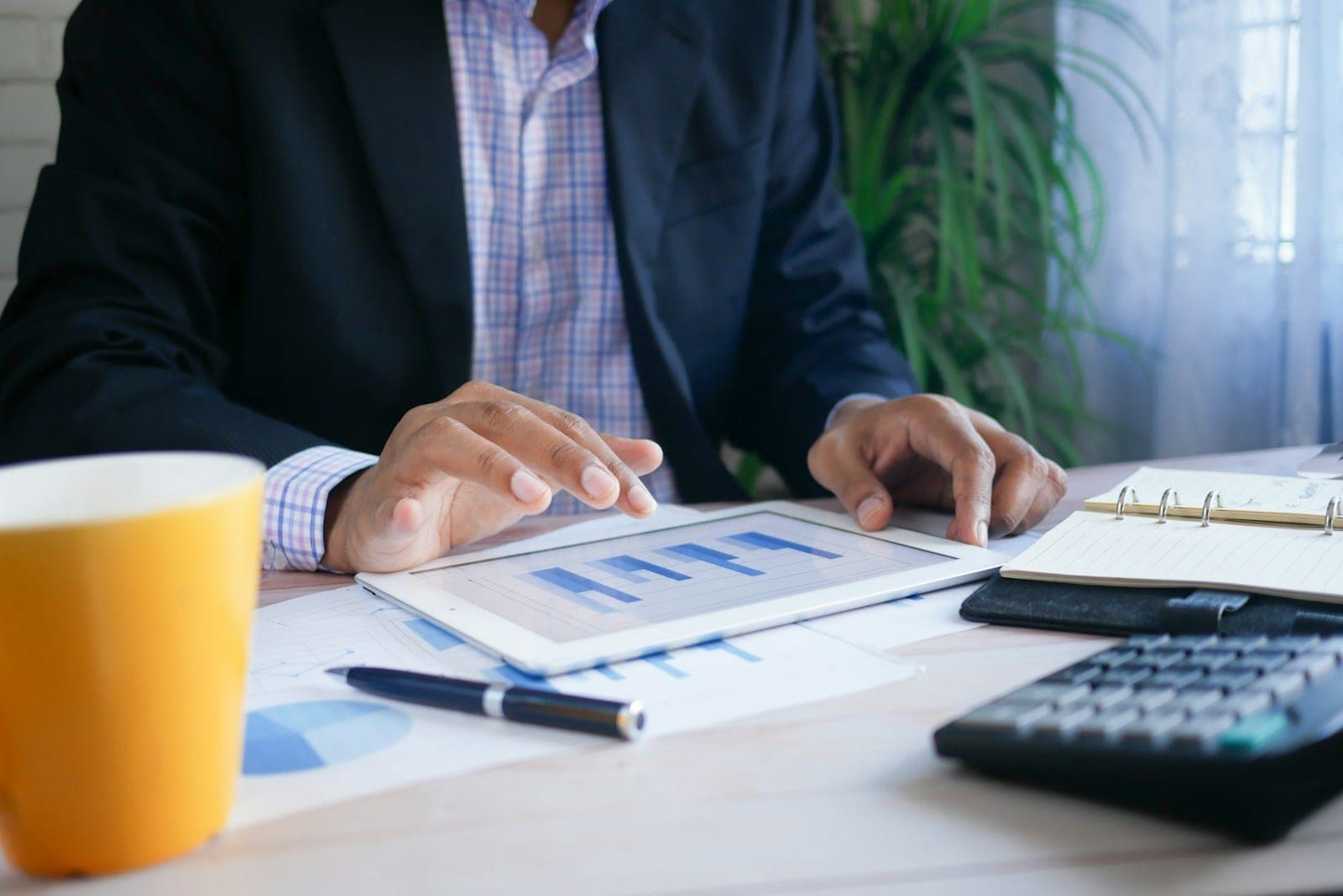 A professional in a suit reviewing charts on a tablet beside a calculator